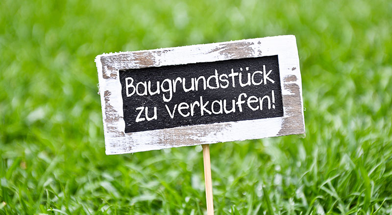 Schild „Baugrundstück zu verkaufen“ auf einer Wiese